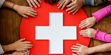 Multiple people's hands holding a first-aid type sign of a red circle with a white cross in the middle