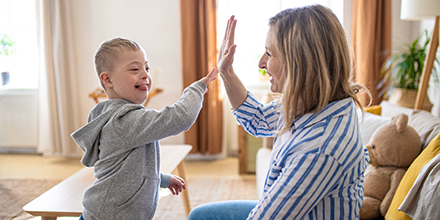 Woman child care provider sharing high-five with young boy with a disability