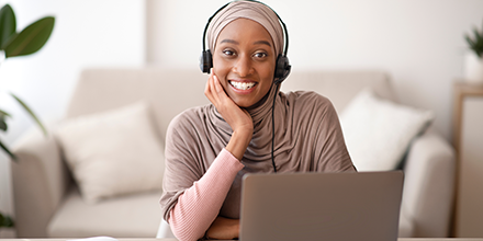 Young, smiling black woman wearing a head scarf working on a laptop computer