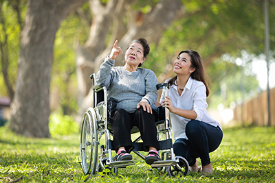 an older woman in a wheelchair outside with a smiling companion