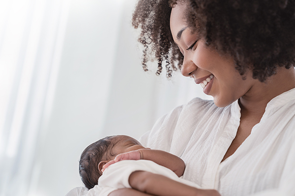 Close up portrait of beautiful young African American mother holding sleep newborn baby in hospital