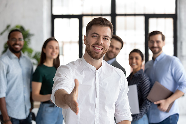 Smiling young Caucasian businessman stretch hand greeting meeting with new office employee or worker, happy male team leader or employer welcome newcomer or intern at workplace, recruitment concept
