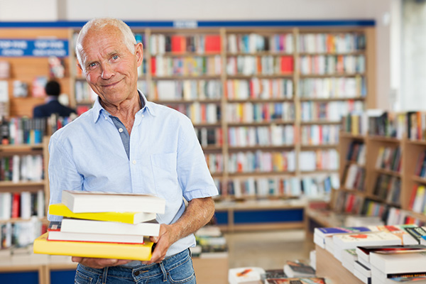 Positive aged man buyer holding pile of books in bookstore