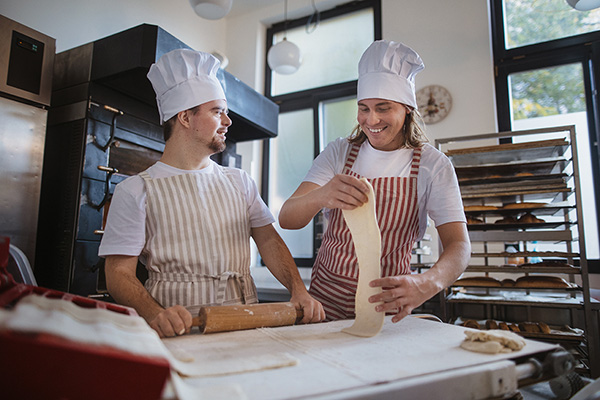 Man with down syndrom helping prepair bread in bakery with his colleague. Concept of integration people with disability into society.