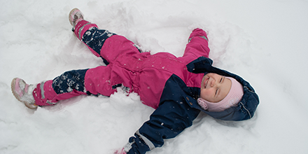 Child in pink and blue snow suit making a snow angel