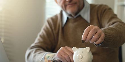 A senior man putting change into a piggy bank.