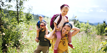 A man and woman holding their son and daughter on their shoulders while hiking.