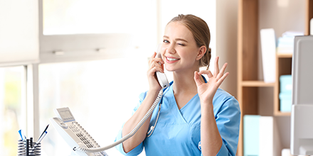 A female health care worker on her work phone giving the 'ok' hand signal.