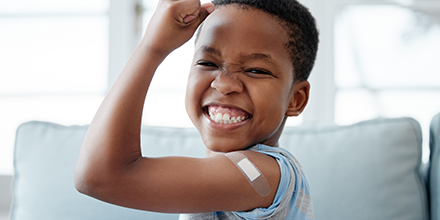 A young boy holding up his arm, smiling, showing a vaccine bandage.