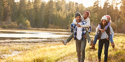 A mother and father giving piggy-back rides to their children on a wilderness hike.