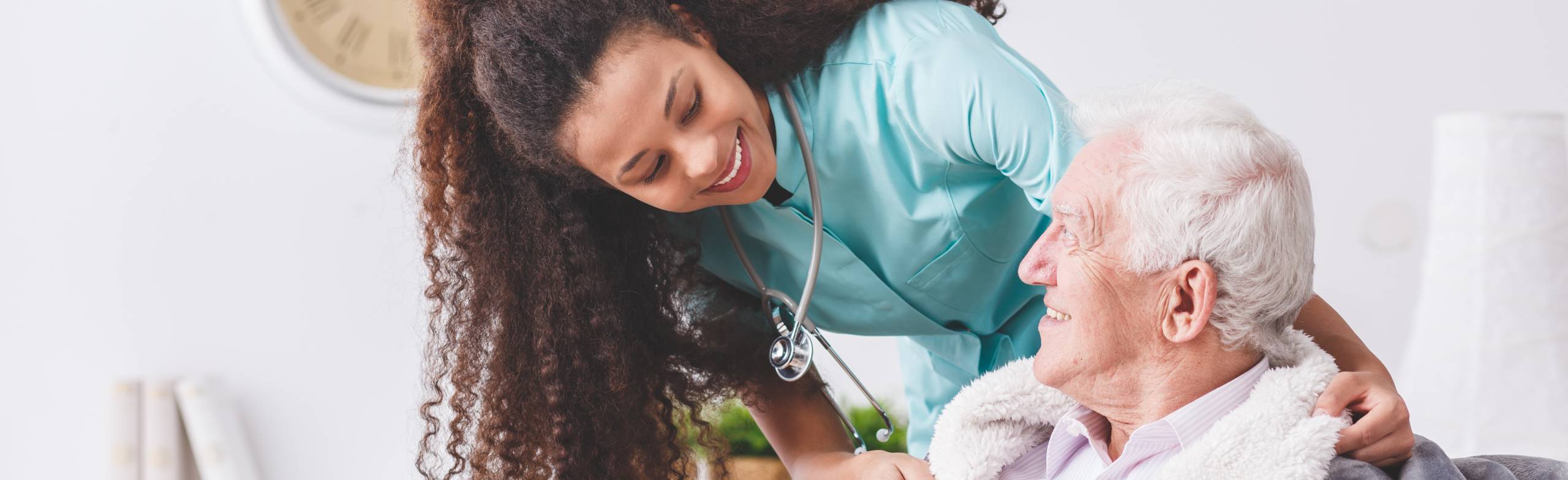A female health care provider smiling as she checks on a senior man.