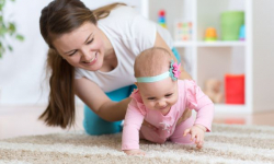woman helping infant girl crawl on the floor