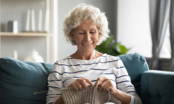 smiling older woman sitting on a blue couch knitting