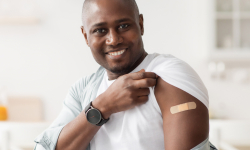 man smiling while showing the bandaid on his arm