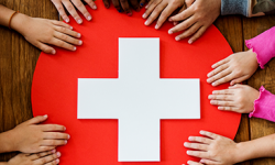 Multiple people's hands holding a first-aid type sign of a red circle with a white cross in the middle