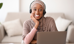 Young, smiling black woman wearing a head scarf working on a laptop computer