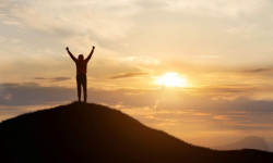 A person stands at the top of a mountain in victory