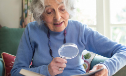 Senior Woman At Home Reading Book Using Magnifying Glass