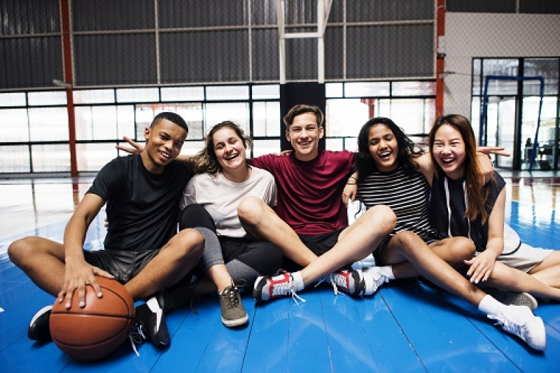 Group of five teens sitting in gym floor with basketball