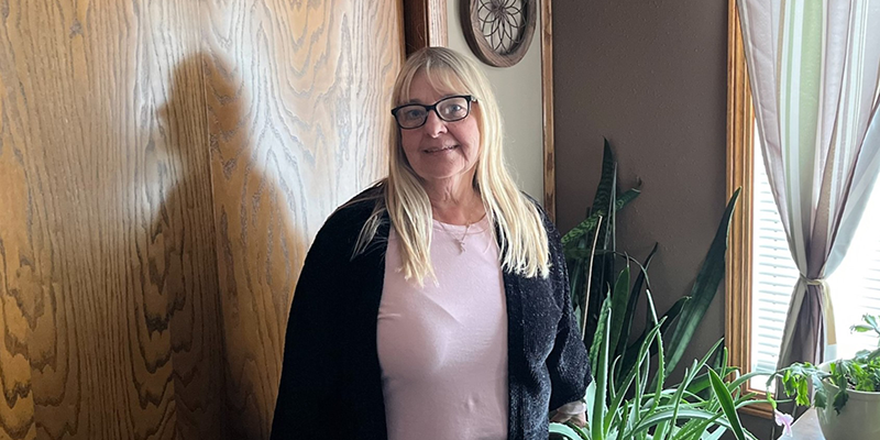 A light skinned female with glasses and blonde hair. She is wearing a pink shirt and a black cardigan.