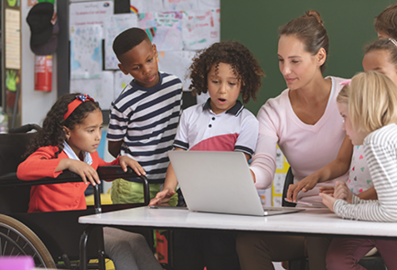 A teacher shows a group of students something on her laptop