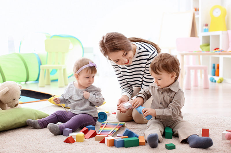 female child care provider playing with little children indoors
