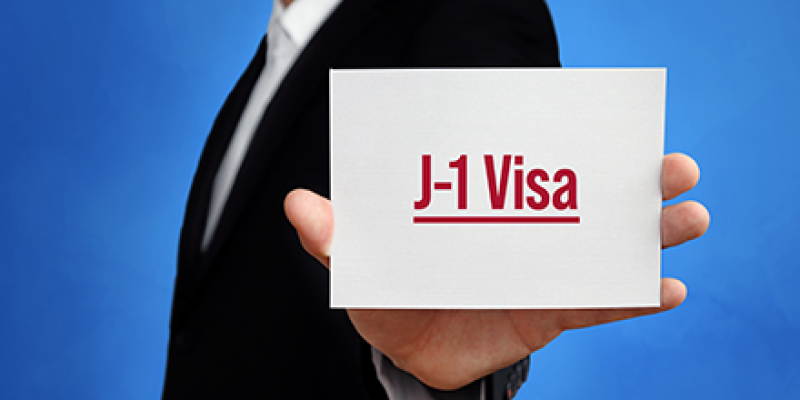 Man holding white card with text J-1 Visa