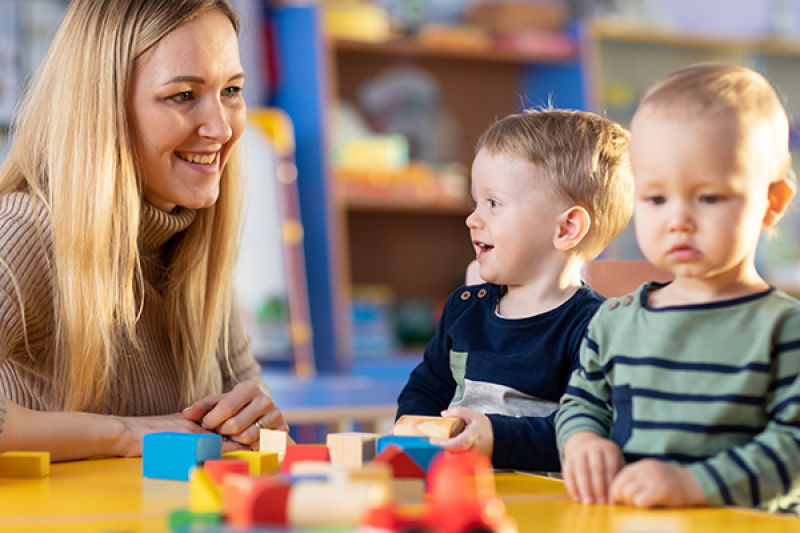 Teacher and cute little girl play with blocks toy in kindergarten
